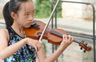 Junge Violinistin spielt ihr Instrument im Freien, unscharfer schöner Hintergrund