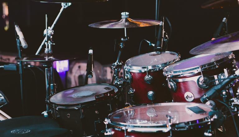 Drumset - ready to be played! Wir schauen von schräg hinten in ein spannende beleuchtetes Drumset. Es ist mikrofoniert und steht in einem Tonstudio oder einer Konzertbühne.