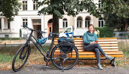 Eine Frau sitzt auf einer Bank in der Hegelallee, neben ihr steht ihr Fahrrad.
