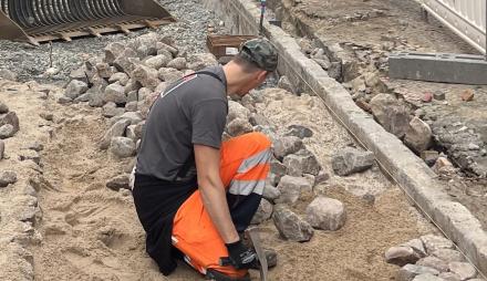 Ein Mann sitzt im Sand und setzt alte Steine, um die denkmalgeschützte Spornstraße zu pflastern.