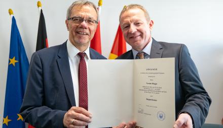 Die beiden Männer Burkhard Exner und Tobias Wiegel stehen nebeneinander und zeigen auf eine Urkunde in DIN-A4-Größe. Es ist die Ernennungsurkunde für den neuen Beigeordneten Tobias Wiegel, der für acht Jahre Beigeordneter der Stadt Potsdam sein wird.