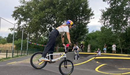 Eine Jugendliche steht auf einem BMX-Rad und fährt über die asphaltierte Berg- und Tal-Bahn, die Pumptrack genannt wird.