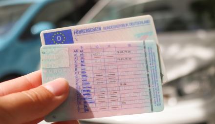 Führerscheine werden vor einem Auto in die Kamera gezeigt.