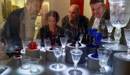 Vier Personen schauen in eine Vitrine, in der barocke Potsdamer Gläser ausgestellt werden.