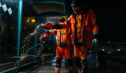 Mitarbeiter der Stadtentsorgung streuen Granulat gegen die Glätte an Haltestellen.