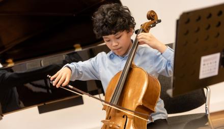Ein sehr junger Cellist spielt engagiert sein Cello. Das Bild steht etwas schief und wirkt dadurch sehr dynamisch
