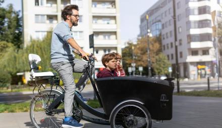 Ein Mann fährt auf einem Lastenrad mit Kindern vorne im Kasten.