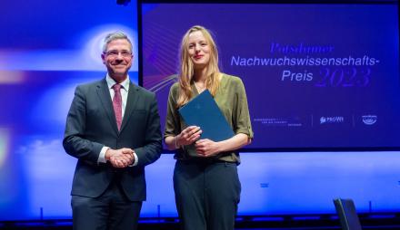 Bei der Verleihung des Nachwuchswissenschafts-Preises 2023 stehen Oberbürgermeister Mike Schubert und die Preisträgerin Dr. Lisa Schwetlick gemeinsam strahlend auf der Bühne. 