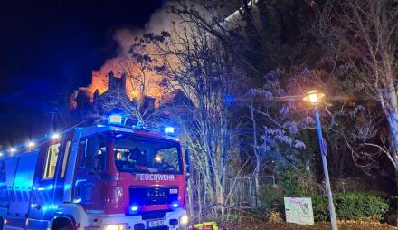 Ein Feuerwehrauto steht vor der brennenden Villa.