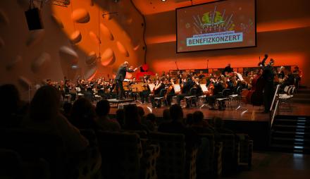 Auf der spektakulären Bühne des Nikolaisaal dirigiert ein Mann ein großes Orchester. Zur Linken sehen wir im Dunkeln sehr viel Publikum.