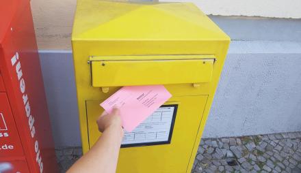 Eine Hand steckt einen Wahlbrief in einen Briefkasten.