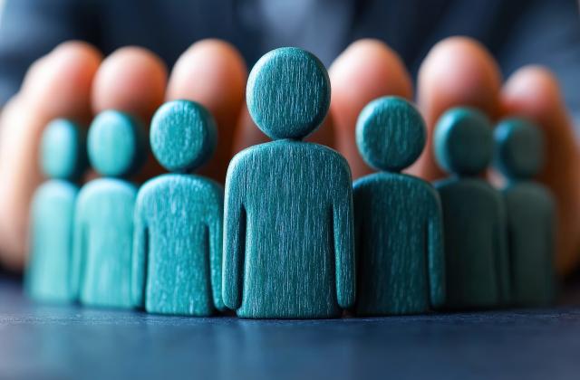 Blaue Holzfiguren mit schützenden Händen darüber.