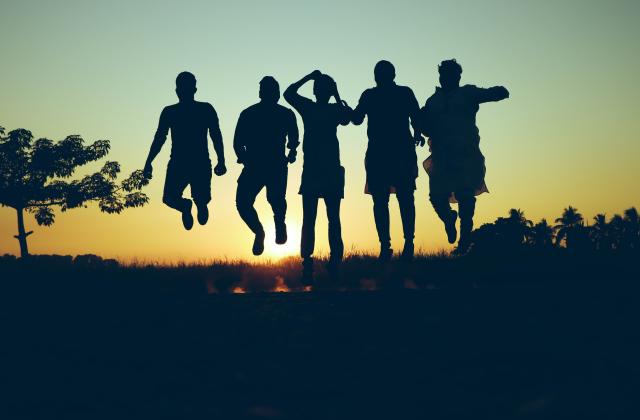 Silhouetten junger Erwachsener mit Lagerfeuer und Sonnenuntergang