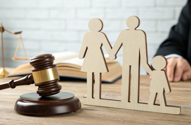 Das Bild zeigt einen Gerichtshammer sowie eine Gerichtswaage sowie Figürchen einer Familie