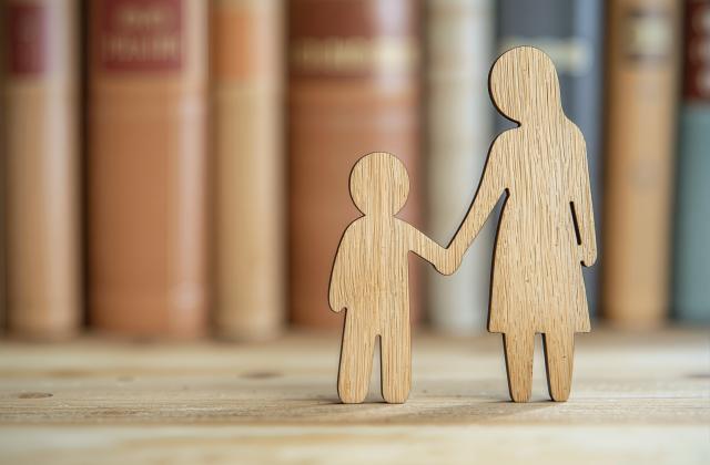Sorgerecht Begleitendes Bild zum Thema Sorgerecht: Symbolische Figur eines Kindes an der Hand eines Elternteils vor dem Hintergrund von Gesetzestexten