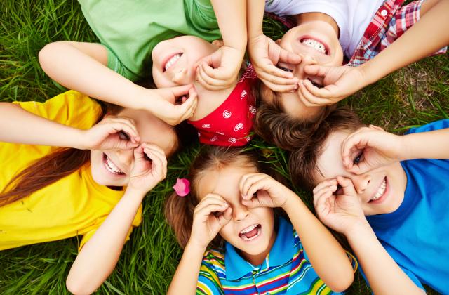 Fünf Kinder liegen in einem Kreis auf dem Rücken und schauen in die Luft.