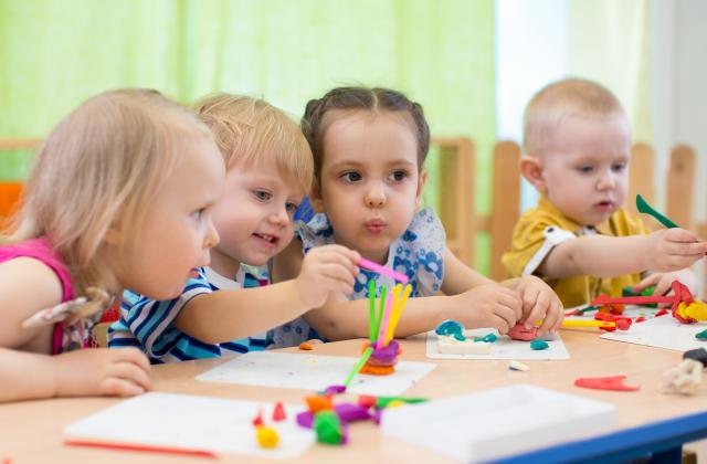 Vier Kita-Kinder sitzen an einem Tisch und basteln mit bunter Knete.