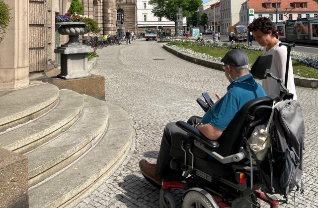Das Foto zeigt einen Rollstuhlfahrer mit der Beauftragten für Menschen mit Behinderung, Dr. Tina Denninger