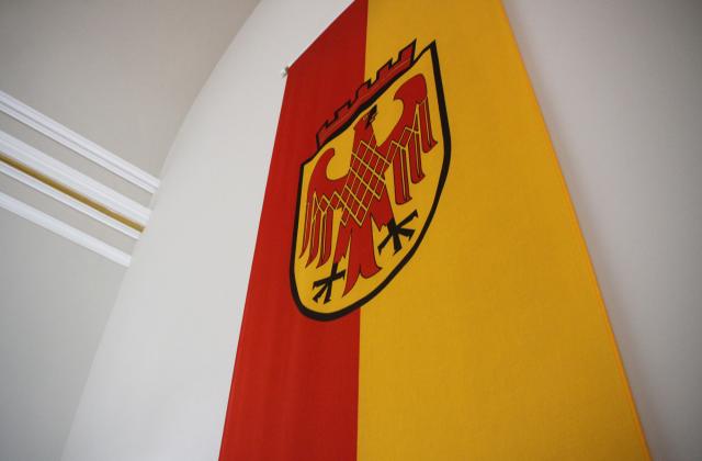 Das Bild zeigt die Flagge der Landeshauptstadt Potsdam: ein roter und gelber Streifen, in der Mitte das Stadtwappen - einen roten Adler auf goldenem Grund.