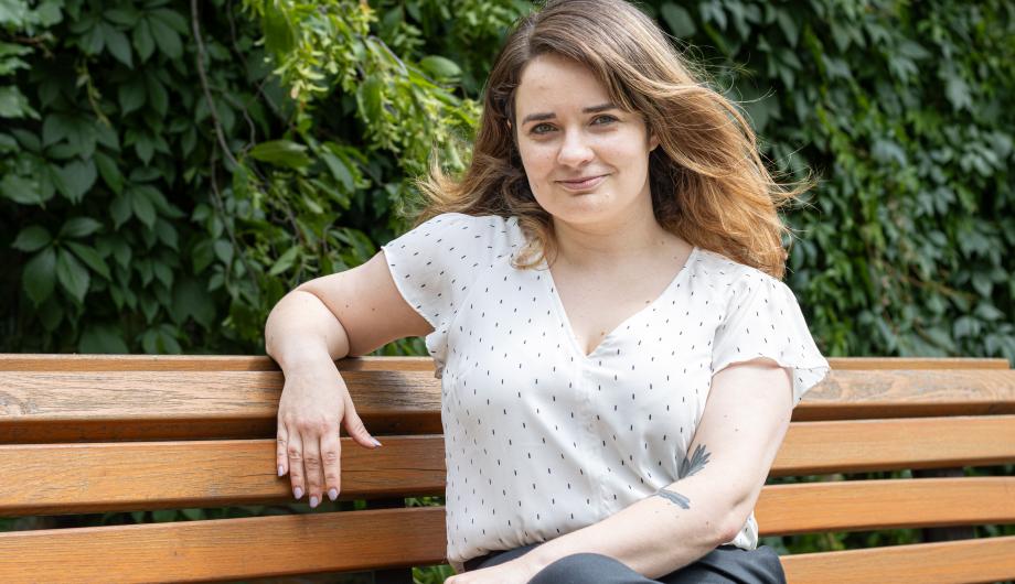 Die Gleichstellungsbeauftragte und Leiterin des Büros für Chancengleichheit und Vielfalt Claudia Sprengel sitzt auf einer braunen Brank, im Hintergrund ist eine grüne Hecke