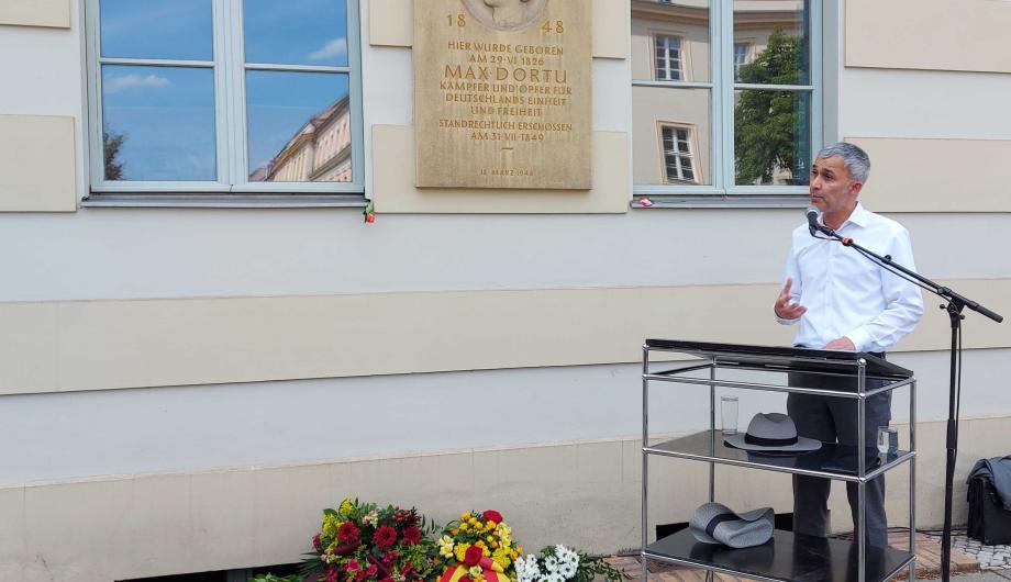 Der Beigeordnete Prof. Walid Hafezi spricht eine Gedenkrede anlässlich des 175. Todestages von Max Dortu und steht vor dem Geburtshaus des Freiheitskämpfers in der Dortustraße.