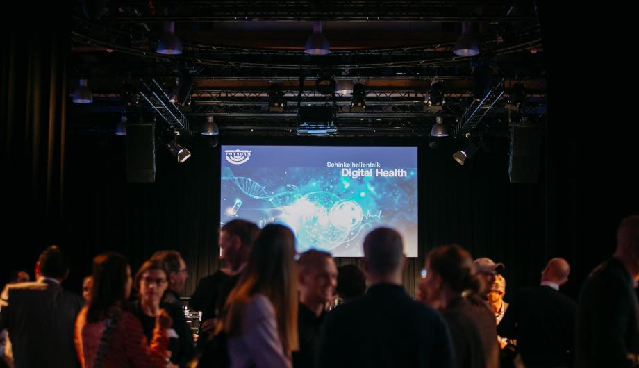Schinkelhallentalk Digital Health - Sall mit Teilnehmenden und Präsentation auf einer Leinwand