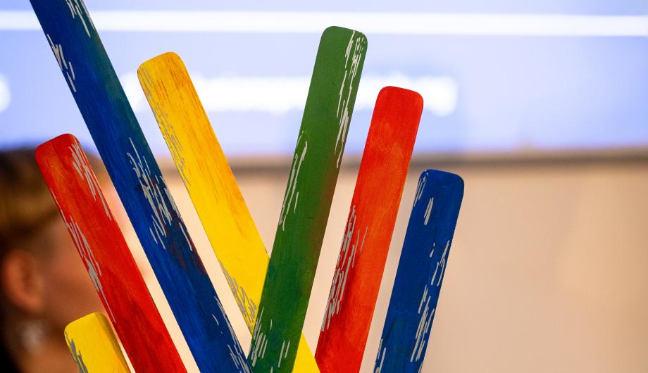 Der Inklusionspreis 2025 der Landeshauptstadt Potsdam: Eine farbenfrohe Skulptur aus bunten Holzstäben in Blau, Gelb, Grün und Rot, die fächerförmig nach oben ragen und auf einem schwarzen Sockel stehen.