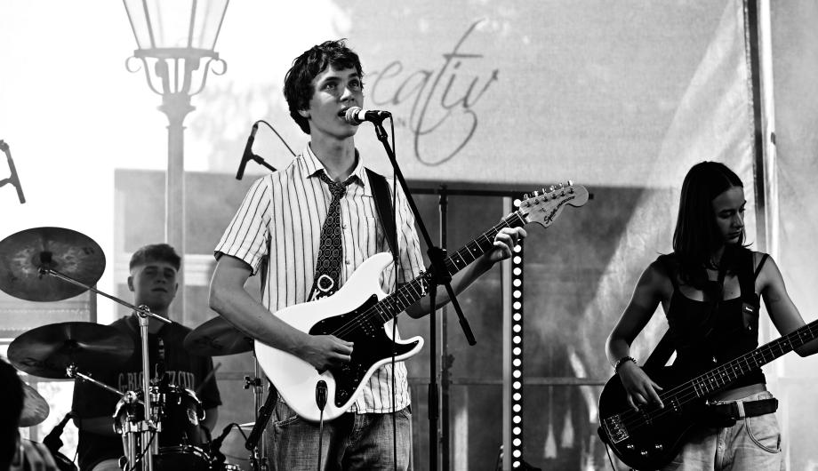 Ein jugendliches Indietrio spielt auf einer Bühne. Das Bild ist stimmungsvoll in schwarzweiss.