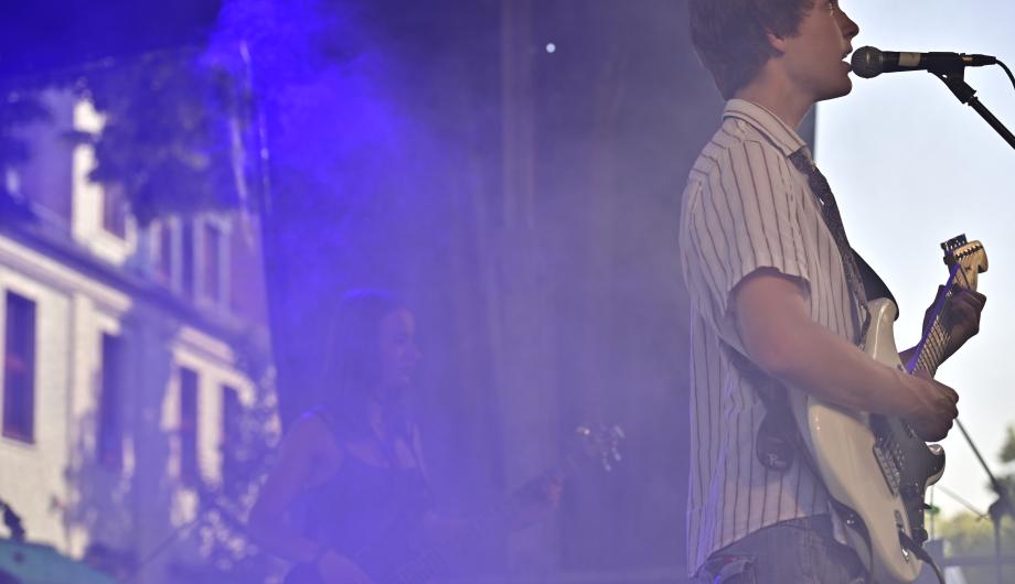 Auf bunter Rockbühne sehen wir von der Seite einen Gitarristen und eine Bassistin
