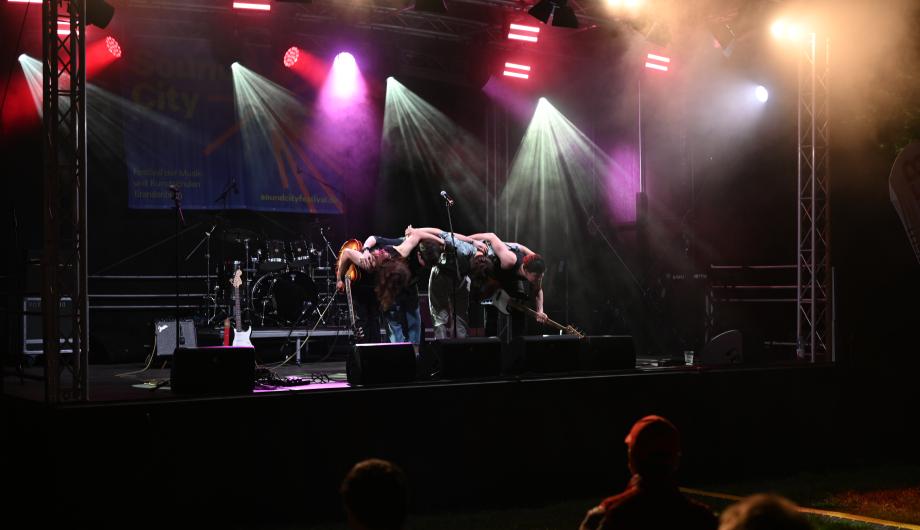 Eine Rockband mit 4 jungen Männern performed auf professionell beleuchteter Bühne verbeugt sich vor dem Publikum