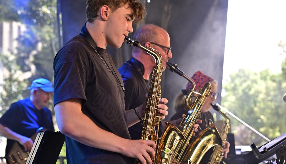 Von der Seite sehen wir einen jungen Saxophonisten - dahinter zwei ältere Saxophonist*innen und einen Bassisten