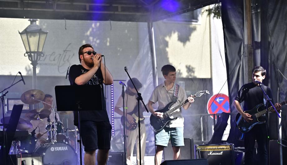 Eine Rockband mit 5 jungen Männern performed auf einer Open-Air Bühne und zeigt dabei Gemeinschaftsgeist