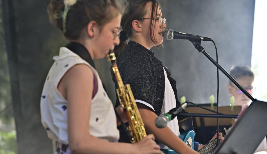 Wir sehen eine sehr junge Saxophonistin, eine singende Gitarristin und einen Keyboarder beim Auftritt