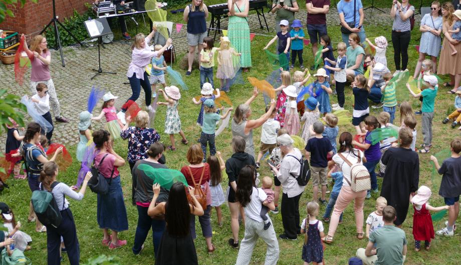 Auf einer Wiese tanzen Erwachsene und Kinder mit Tüchern