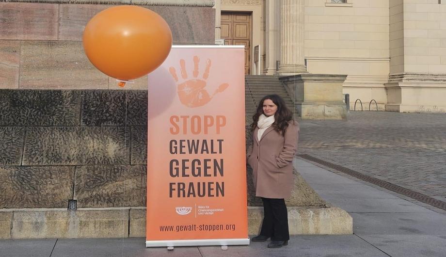 Claudia Sprengel steht neben einem orangefarbenen Banner mit der Aufschrift „Stopp Gewalt gegen Frauen“. Vor ihr und im Hintergrund sind große orangefarbene Ballons Teil der Installation am Alten Markt in Potsdam.