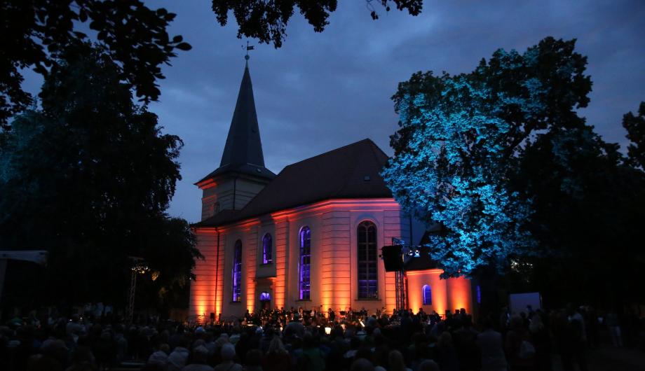 Das Foto zeigt die Musiker des Sinfonieorchesters Collegium musicum Potsdam 2016 vor der illuminierten Friedrichskirche auf dem Weberplatz in Babelsberg.