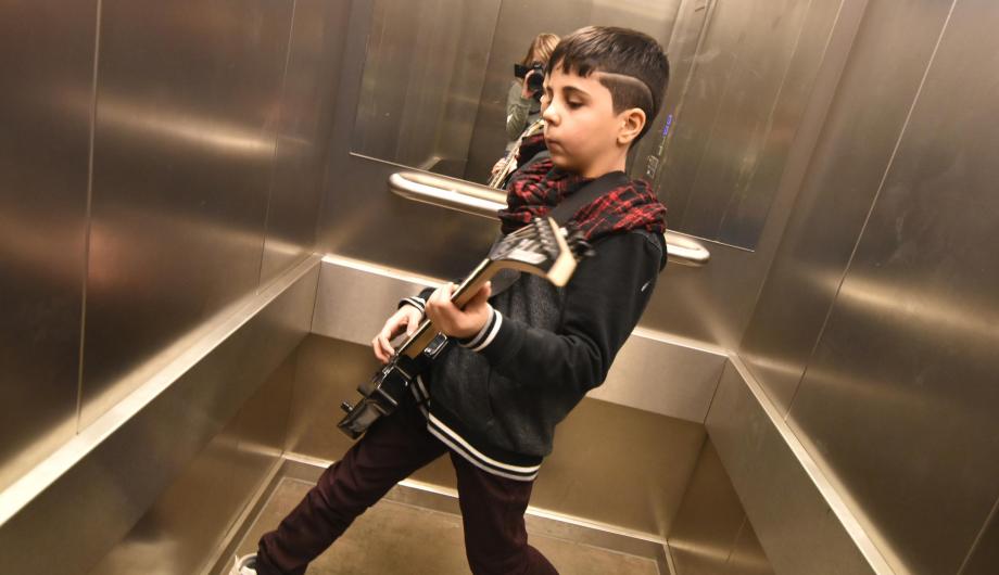 Ein Junge posiert mit E-gitarre in einem Aufzug. Er wirkt selbstbewußt und in sein vorgetäuschtes Spiel versunken.
