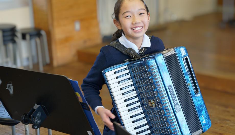 Ein asiatisch aussehendes Kind strahlt in die Kamera und spielt ein blaues Akkordeon