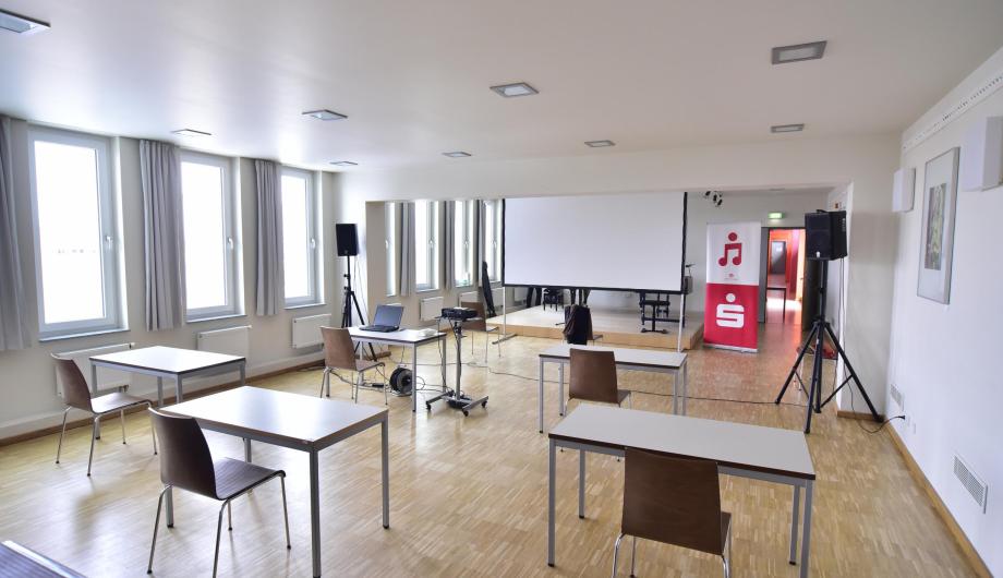 Jugend Musiziert Wettbewerb Hybrid 2021 Tische, Stühle und eine BEamerleinwand sind für eine Hybridveranstaltung des Wettbewerbes Jugend Musiziert in einem Raum der Musikschule am Campus am Stern aufgebaut.
