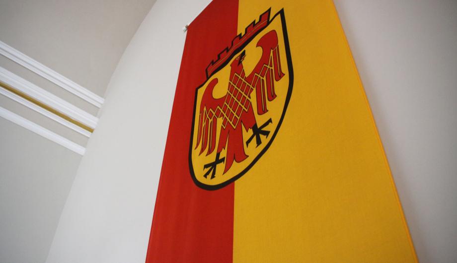 Das Bild zeigt die Flagge der Landeshauptstadt Potsdam: ein roter und gelber Streifen, in der Mitte das Stadtwappen - einen roten Adler auf goldenem Grund.