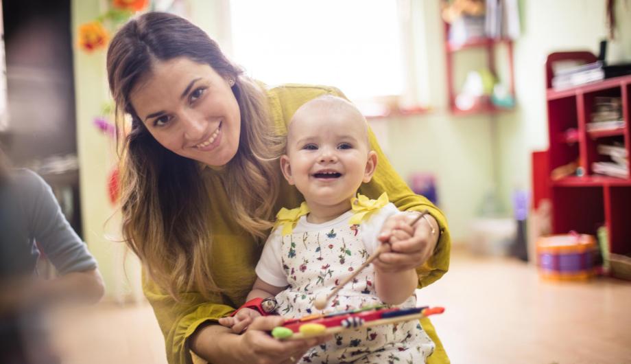 Baby spielt auf Glockenspiel in Arm seiner Mutter