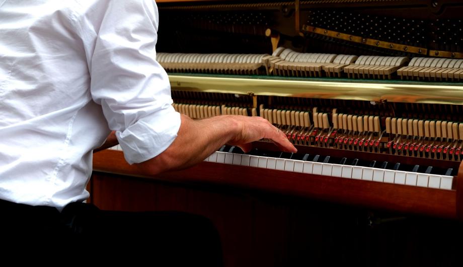 Blick auf die Hände eines Pianisten und das geöffnete Klavier. Das sieht nach Jazz oder Popmusik aus.