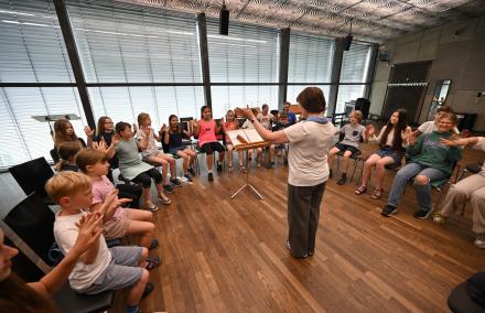 Ein Kinderchor sitzt im Kreis und macht fröhliche Bewegungen zur Musik.