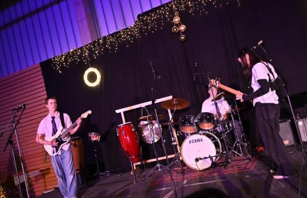 Auf einer Bühne spielen ein Gitarrist, eine Bassistin und ein Schlagzeuger.