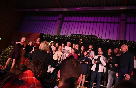 Ein Erwachsenen Chor singt auf einer Bühne. Links im Bild spielt eine Violinistin.