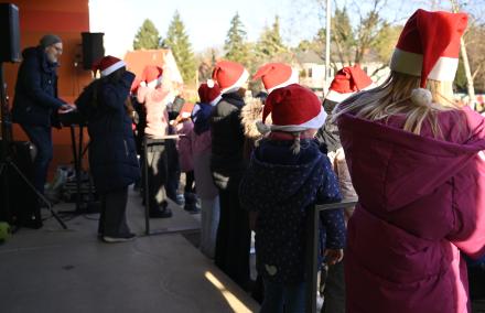 Wir sehen den Rücken vieler Kinder - alle tragen eine Weihnachtszipfelmütze. Sie singen gerade für ihre Klassenkameradinnen und -kameraden.