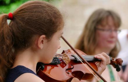 Bühnenprobe mit Violine Einer jungen Geigerin über die Schulter geschaut. Sie blickt zu ihrer Klavierbegleiterin im Hiintergrund