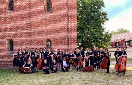 Streichorchester STRINGendo der Städtischen Musikschule Potsdam Ein jugendliches Streichorchester posiert vor der hohen Backsteinmauer eines vielleicht kirchlichen Gebäudes mit Instrumenten.