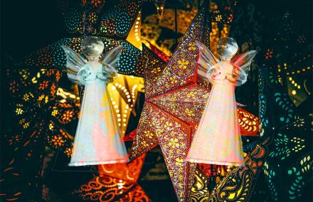 Zwei transparente Glasengel schweben vor rot und gelb leuchtenden Papiersternen