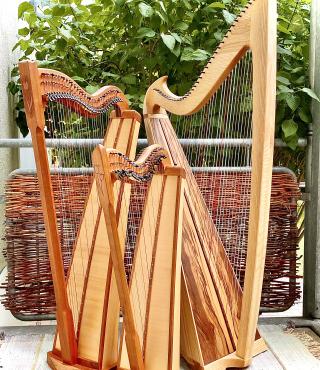 Auf einem Balkon sind 3 verschiedenen große Harfen positioniert. Ihre Hölzer leuchten warm.